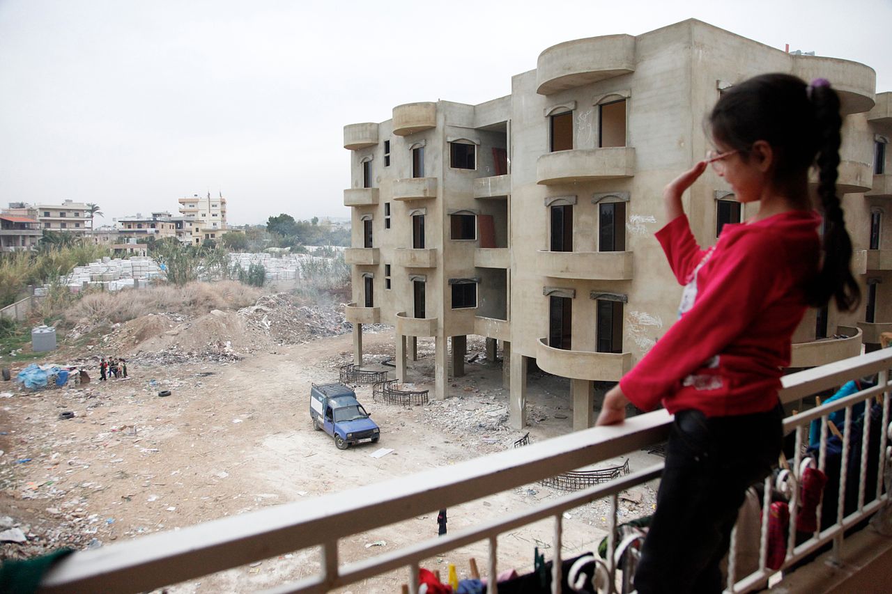 a_syrian_girl_waves_from_the_balcony_of_an_unfinished_apartment_block_in_northern_lebanon_11173940763
